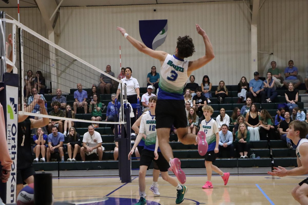 Senior Jace Hoffman spikes the volleyball over the net as junior Aidric Bernd and freshman Henry Meyer watch in anticipation. The high school boys' season wrapped up in a two-set win over Lawrence High School.